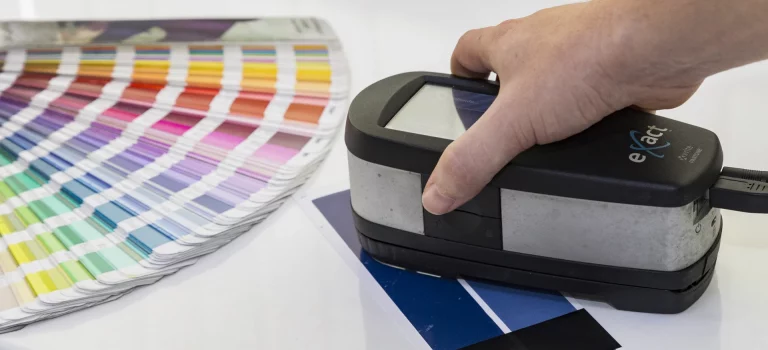 Espectrofotómetro X-Rite eXact midiendo color en impresión junto a guía Pantone.