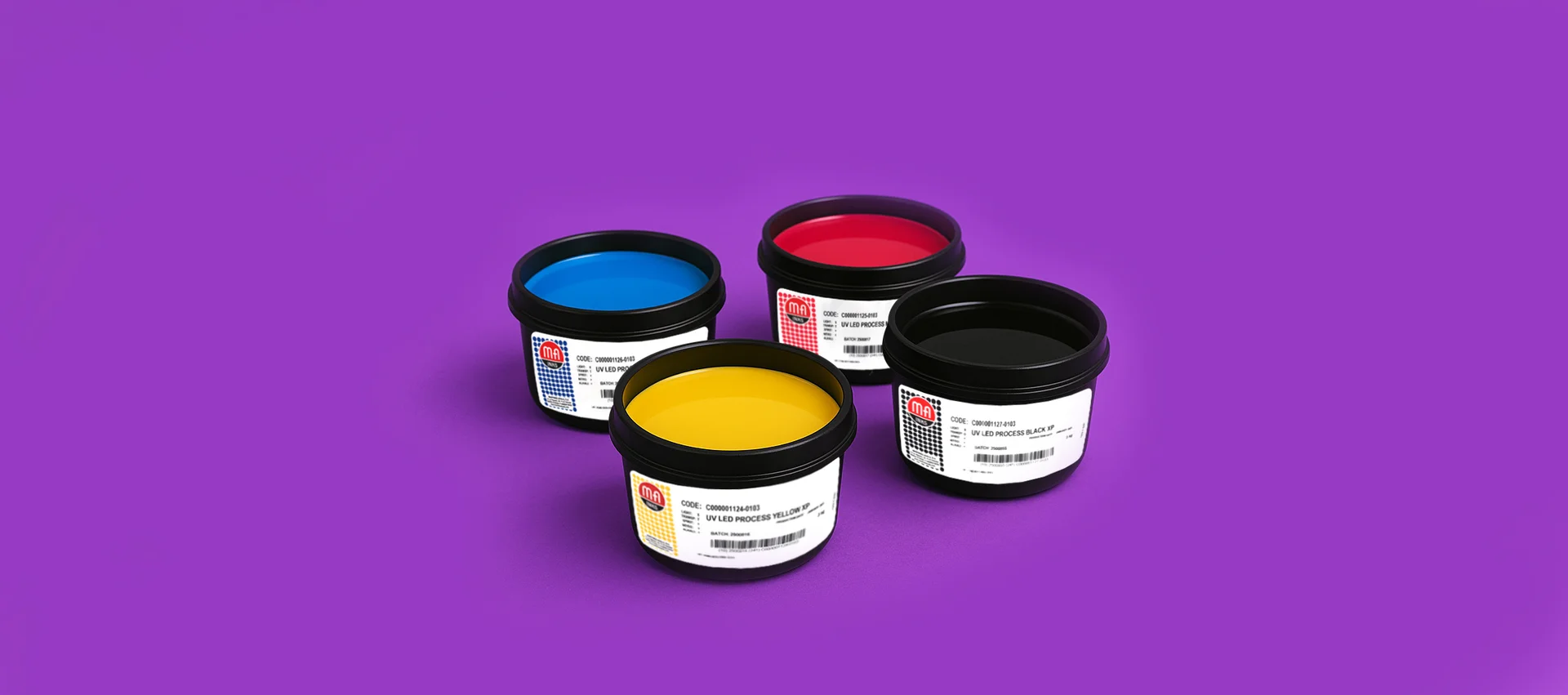 Tarrinas de tinta offset MA Inks en colores CMYK (cian, magenta, amarillo y negro) sobre fondo morado, utilizadas en impresión profesional.